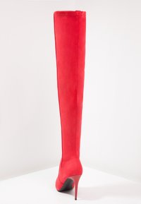 Røde over-knæ støvler lavet af ruskind, med et elegant design, stilethæle og glat tekstur. Syninger langs bagsiden.