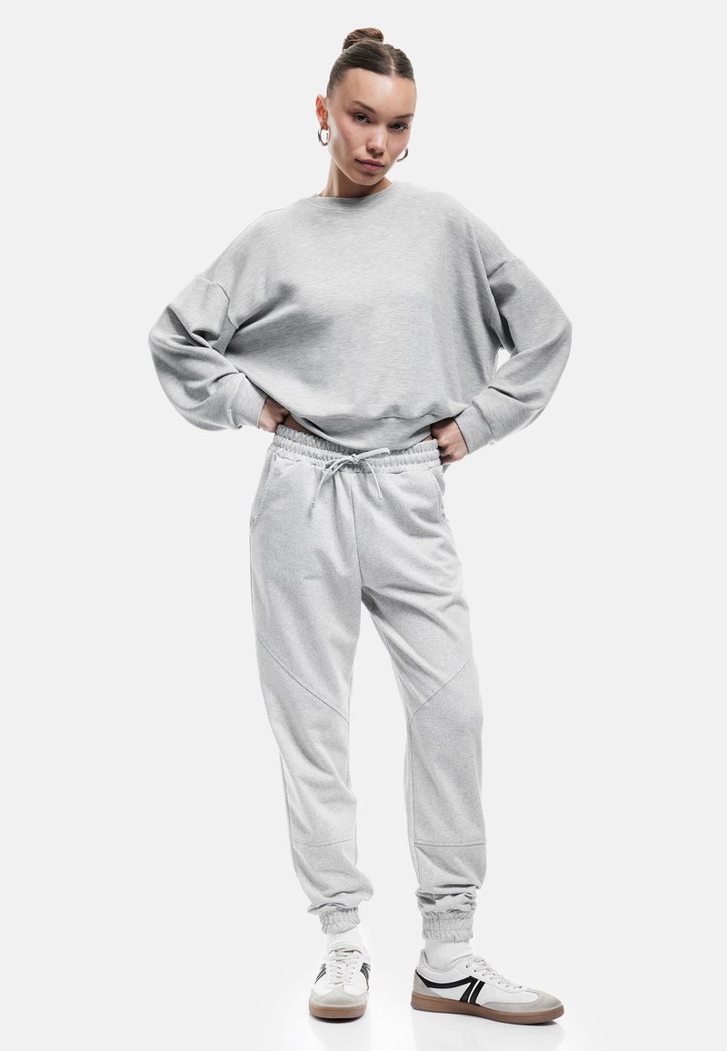 Lys grå oversized sweatshirts med dropped shoulders, parret med tapered grå sweatpants med elastisk talje og manchetter.