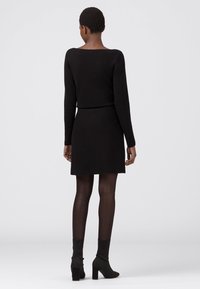 Svart stickad klänning med långa ärmar och figurnära silhuett, i kombination med svarta opaqua strumpbyxor och klackade ankelstövlar.