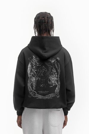 Crna dukserica s velikom bijelom grafikom koja prikazuje anđeosku figuru i dekorativne elemente na leđima, napravljena od mekanog materijala.