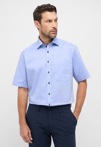 Camicia a maniche corte azzurro chiaro con colletto button-down, taschino frontale e bottoni blu scuro. Realizzata in un tessuto liscio, vestibilità aderente.
