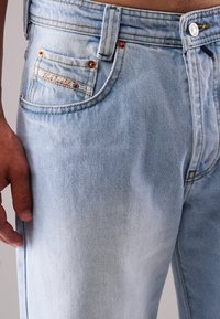 Helle blaue Jeans aus Denim mit einem ausgewaschenen Finish, ausgestattet mit Kupfennieten, einer Vordertasche und einem Markenpatch über der Gesäßtasche.
