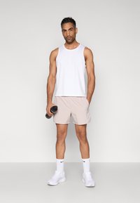 Valge varrukateta top ja helebeež lühikesed püksid, musta joogipudeliga, valgete spordijalatsite ja sokkidega. Sile kangas, vabaaja disain.