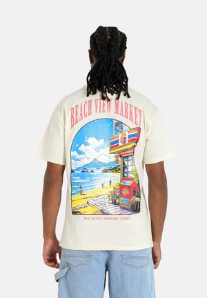 Crème-kleurig t-shirt met een kleurraf tische afbeelding van een strandscène met een markt en bergen op de achtergrond. Casual fit en korte mouwen.