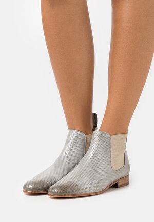 Bottines en cuir argenté avec un design perforé et des panneaux élastiques beiges sur les côtés ; talon plat en bois ; texture lisse et bout rond.