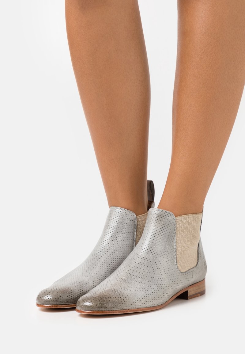 Botas de tobillo de cuero plateado con diseño perforado y paneles laterales elásticos en beige; tacón de madera plano; textura suave y puntera redondeada.