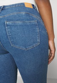 Mørkeblå denimjeans med medium livhøyde, med baklomme og en brun lærlabel på livlinjen. Glatt tekstur og klassisk design.
