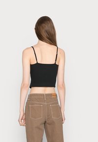Top cropped preto com alças finas, visto de costas, combinado com calças de cintura alta castanho claro com costuras à vista e bolsos.