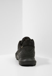 Czarne buty do wędrówek z teksturowaną cholewką, wzmocnionym piętrem i gumową podeszwą. Posiadają pętelkę do łatwego zakładania oraz szczegóły wodoodporne.