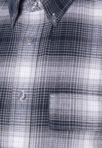 Camisa de cuadro que presenta una mezcla de colores azul marino, gris y blanco. Botones en plata, con un bolsillo en el pecho. La tela tiene una textura tejida.