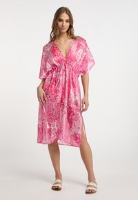 Rožinė gėlių raštų kimono suknelė su plačiomis rankovėmis, giliu V formos iškirpimu ir raišteliu juosmens srityje, pagaminta iš lengvos, permatomos medžiagos.