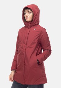 Giacca impermeabile rossa con cappuccio, dotata di una chiusura frontale con zip, tasche laterali e un logo minimalista sul petto. Tessuto liscio, design di lunghezza media.