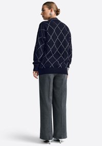 Merevaigist sinine kudum, millel on valge rombikujuline muster, soonikuga varrukad, lõdva lõikega, sobib hallide laienevate pükstega ja hõbedaste kontsakingadega.