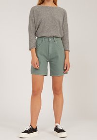 Light green denim shorts with a high waist, paired with a black and white striped long-sleeve shirt. Worn with black sneakers.