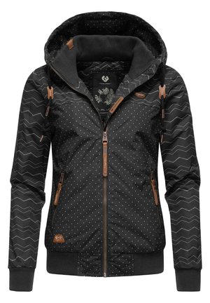 Zwarte dameshooded jas met witte polkadots, zigzagpatroon mouwen, rits aan de voorkant en bruine leren ritslipjes en accenten.
