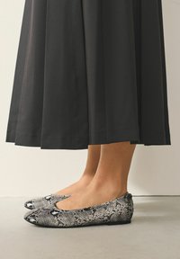 Sort nederdel over anklen og flade sko med slangeskindsprint i sort og hvid, med flad sål og rundet tådesign.