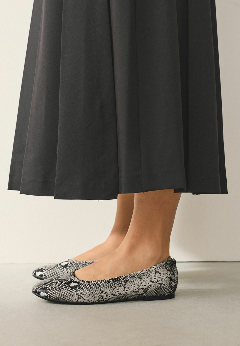 Sort nederdel over anklen og flade sko med slangeskindsprint i sort og hvid, med flad sål og rundet tådesign.