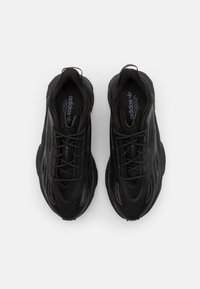 Black athletic sneakers with a textured upper, chunky sole, and prominent lacing system. Features reflective accents and branding on the tongue.