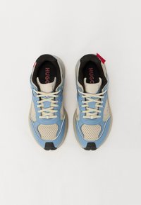 Baskets bleu et beige avec tige en mesh et synthétique, doublure noire, lacets plats et accents rayés. Logo rouge sur le talon. Semelle en caoutchouc plate.