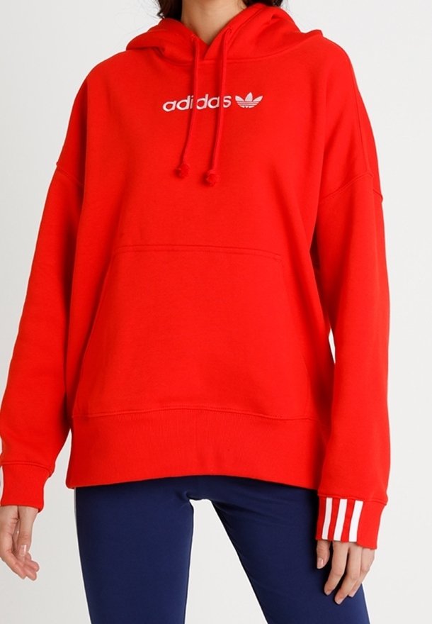 Sudadera con capucha roja hecha de algodón, con un bolsillo frontal y el logo "adidas" en blanco. Presenta puños a rayas y un ajuste relajado.