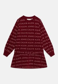 Vestido de sweatshirt cor burgundy com mangas longas, apresentando o texto repetido em branco "CALVIN KLEIN JEANS" numa fonte moderna. Textura de tecido suave.