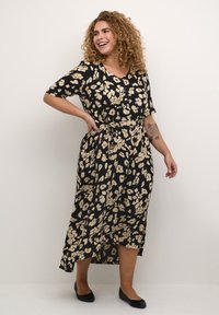 Vestido negro con un patrón floral en tonos crema, mangas cortas, escote en V y un lazo en la cintura, con una silueta fluida hasta los tobillos.