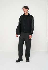 Fekete és szürke dzseki bőr ujjal, gombos záródással, fekete felsőre húzva, szürke nadrággal és fekete cipővel párosítva. Egyszerű dizájn.