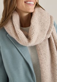 Ljusrosa, texturerad halsduk lager på lager över en ljusgrå tröja, kompletterad av en blå kappa med en slät yta. Mjuk och mysig utstrålning.