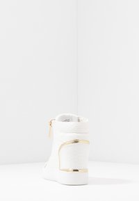 Vit, texturerad ankelsneaker med en guldaccent på hälen och dragkedjan. Har en mjuk textilfoder och en gummisula.