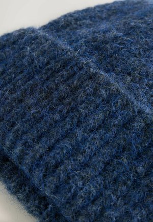 Tejido de lana azul de punto con texturas variadas; presenta una mezcla de fibras azules oscuras y claras, creando una apariencia difusa y un patrón acanalado.