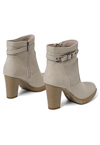 Stivaletti beige alla caviglia con design perforato, tacco alto a blocco e dettaglio con fibbia. Chiusura con cerniera laterale, texture liscia.
