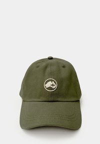 Gorra color caqui con forma estructurada, visera curva y logo bordado en un parche circular. El material parece algodón texturizado.