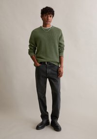 Pulover verde cu dungi, blugi negri cu curea și cizme negre. Puloverul are mâneci lungi și decolteu rotund. Design simplu, casual.