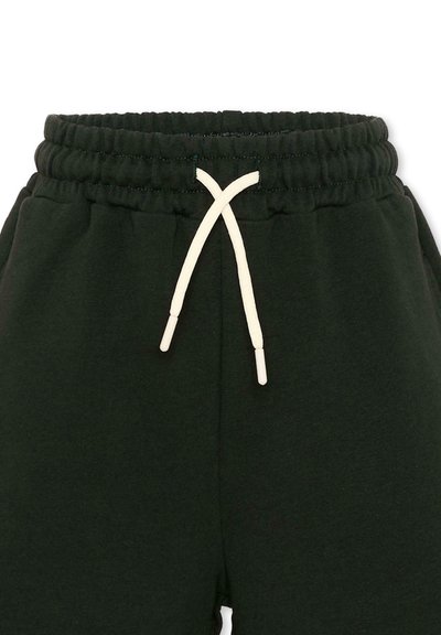 Pantalon de survêtement à taille élastique noire avec cordon blanc noué en un simple nœud au centre avant.