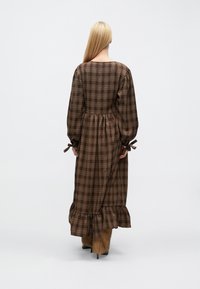 Dlhé hnedé kárované šaty s balónovými rukávmi, zošitým pásom a volánovou sukňou. Rukávy majú stužkové šnúrky na úpravu.