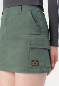 Groene denim rok met een zijzak en een RVCA-logo patch. De stof heeft een gestructureerde afwerking met een aansluitend ontwerp en een rechte zoom.