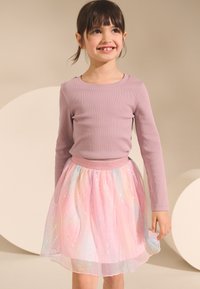Long-sleeve lilac top paired with a light pink, iridescent tulle skirt featuring subtle wavy patterns, elastic waistband, and shiny accents.