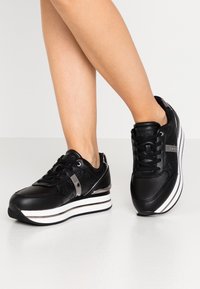 Czarne sneakersy z cholewką ze skóry, z fakturowanym wykończeniem, błyszczącymi srebrnymi akcentami i grubą białą podeszwą. Posiadają czarne sznurowadła i logo.