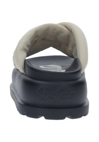 Des sandales Buffalo avec une tige beige douce, une épaisse semelle noire et un marquage en relief. Le design est minimaliste sans matériel visible.