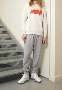 Vitt sweatshirt med röd "JORDAN"-tryck, tillsammans med gråa sweatpants och vita sneakers med genomskinliga sulor. Mjuk textur, avslappnad passform.