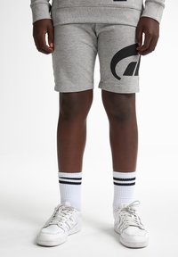 Shorts en coton gris avec un logo noir sur le côté, associés à des chaussettes blanches avec des rayures noires et des baskets blanches.