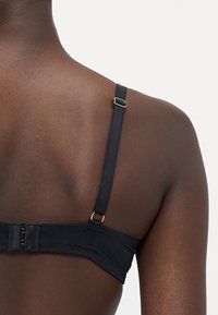 Sort bh med justerbare stropper, der har en krog-og-øje lukning og en subtil tekstureret stof. Hardware i guldfarve. 