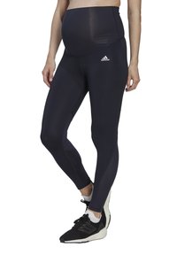 Leggings da maternità neri con vita alta, caratterizzati da una consistenza liscia e un branding discreto. Abbinati a scarpe da ginnastica nere.
