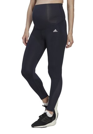 Černé těhotenské legíny s vysokým pasem, mají hladký povrch a jemné logo. Spárováno s černými sportovními botami.