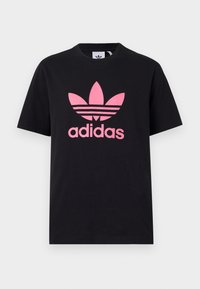 Svart bomull T-skjorte med et stort rosa Adidas-logo med tre striper over. Rund hals og korte ermer. Klassisk passform.