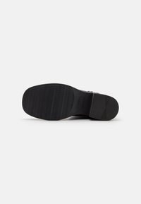 Black shoe sole with a textured pattern. Features flat design and rubber material for grip. Includes a smooth accent area near the heel.