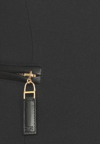 Tessuto nero con chiusura a zip, dotata di un tirante in metallo dorato e un'etichetta in pelle nera. Texture liscia con una finitura opaca.
