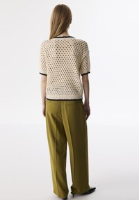 Beige gebreide tops met korte mouwen met een open gaasdesign en zwarte afwerking, gecombineerd met hoog-getailleerde olijfgroene broeken in een relaxte pasvorm.