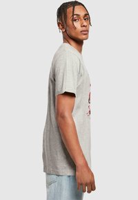 Gray cotton t-shirt with short sleeves and a crew neck. Features a graphic design in red tones on the front. Model stands sideways.
