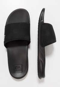 Sandales à glissière noires avec un semelle intérieure texturée, une sangle rembourrée avec découpes, et une semelle en caoutchouc avec un détail logo subtil.